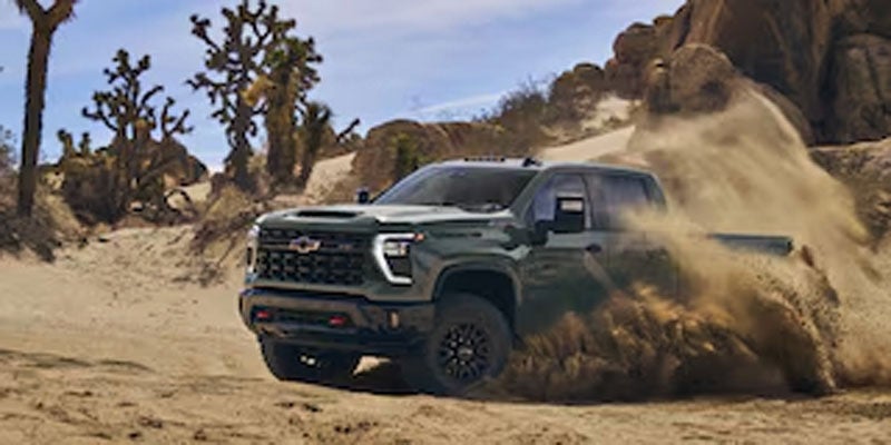 Green Chevrolet Silverado HD pickup truck driving through a dusty off-road trail.