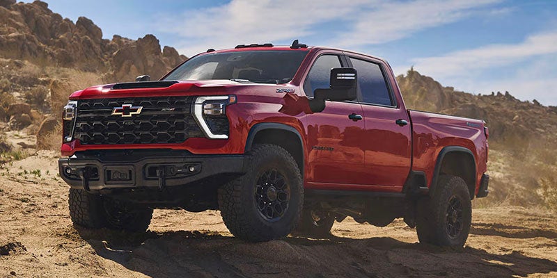 Red Chevrolet Silverado HD pickup truck off-roading on a rocky desert trail.