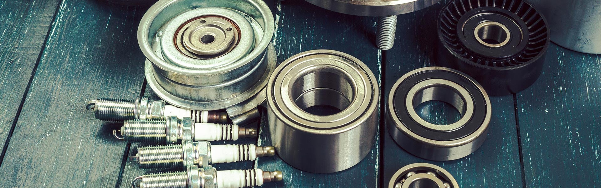 Automotive parts including spark plugs, bearings, and pulleys arranged for a vehicle repair or maintenance service.