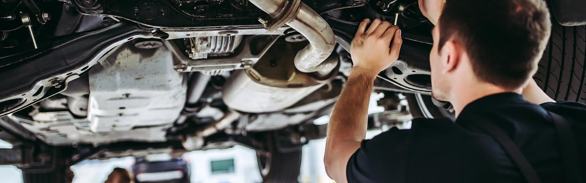 Automotive technician inspecting the underside of a vehicle on a lift in a service garage.